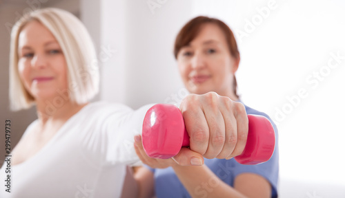 A physiotherapist helps an older woman recover from an injury through exercise with dumbbells.