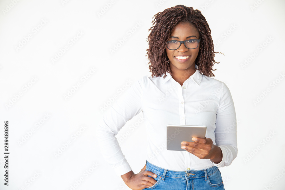 Happy confident expert holding tablet, looking at camera, smiling. Young African American female professional standing isolated over white background. Wireless technology for business concept Happy confident expert holding tablet, looking at camera, smiling. Young African American female professional standing isolated over white background. Wireless technology for business concept