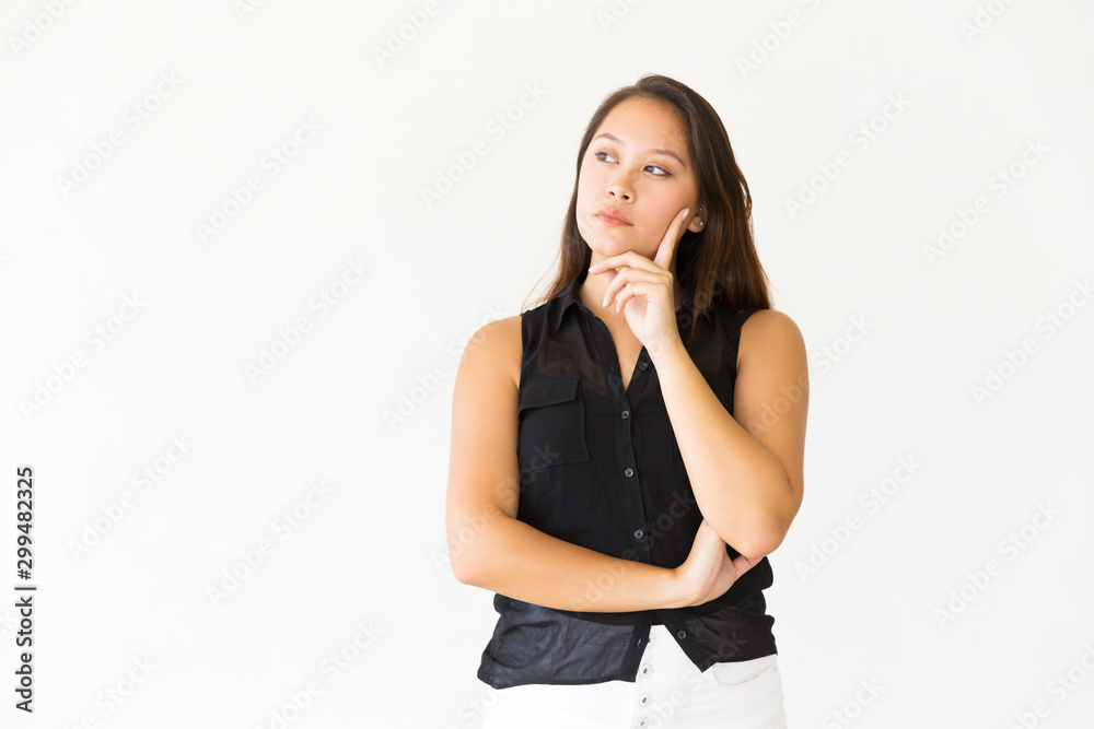 Pensive serious female customer touching face with finger and looking at copy space. Young Latin woman in casual standing isolated over white background. Advertising concept Pensive serious female customer touching face with finger and looking at copy space. Young Latin woman in casual standing isolated over white background. Advertising concept