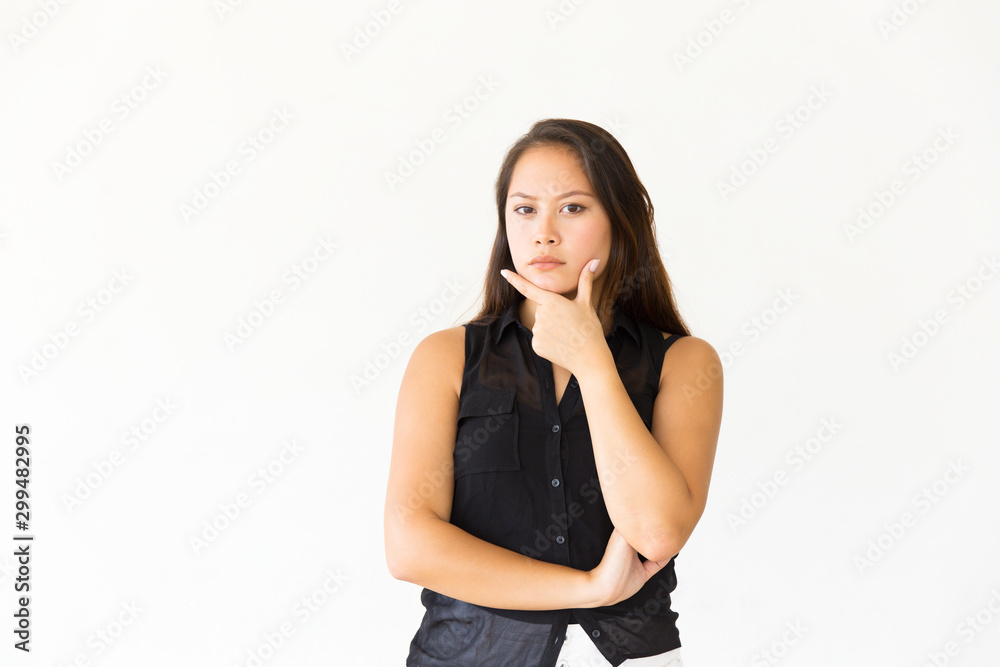 Pensive focused female customer touching chin and looking at camera. Young Latin woman in casual standing isolated over white background. Promotion concept Pensive focused female customer touching chin and looking at camera. Young Latin woman in casual standing isolated over white background. Promotion concept