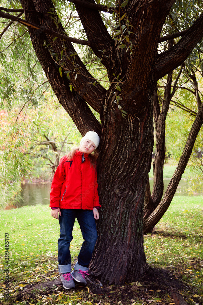 Girl is walking in the Park in autumn and she is standing on the shore of a pond next to a big tree Girl is walking in the Park in autumn and she is standing on the shore of a pond next to a big tree