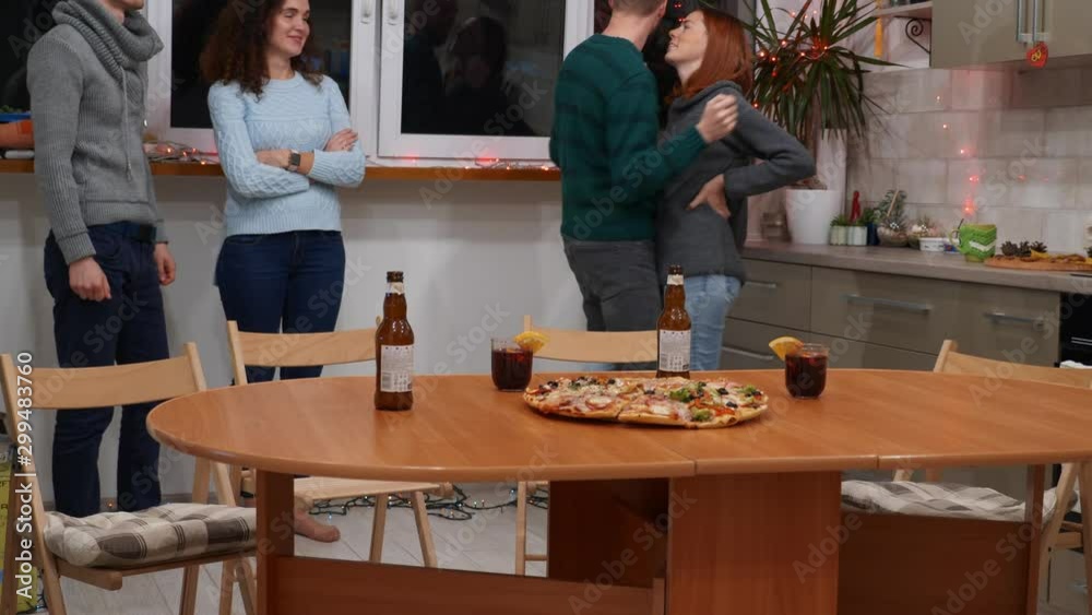 Guys and girls are dancing in the kitchen. Happy friends celebrating new years eve party at home. Pizza, bottles of beer and glasses of mulled wine on the table. Holidays and celebration concept. 4K Guys and girls are dancing in the kitchen. Happy friends celebrating new years eve party at home. Pizza, bottles of beer and glasses of mulled wine on the table. Holidays and celebration concept. 4K
