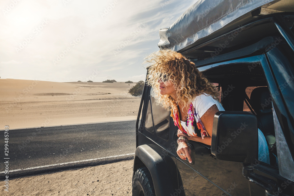 Beautiful blonde curly hair adult young woman outside the car enjoying the travel lifestyle and alternatie vacation with tent on the roof and free camping everywhere - people traveling - desert - obrazy, fototapety, plakaty 