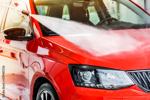 Water jet or high pressure car washing. Manual spray cleaning of red vehicle close up or detail.