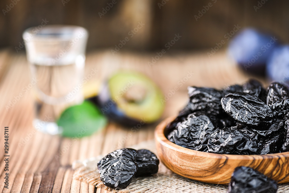 Prunes in wooden bowl on rustic table. Plum brandy or slivovitz in small glass background. Prunes in wooden bowl on rustic table. Plum brandy or slivovitz in small glass background.