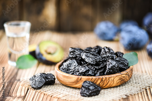 Prunes in wooden bowl on rustic table. Plum brandy or slivovitz in small glass background.
