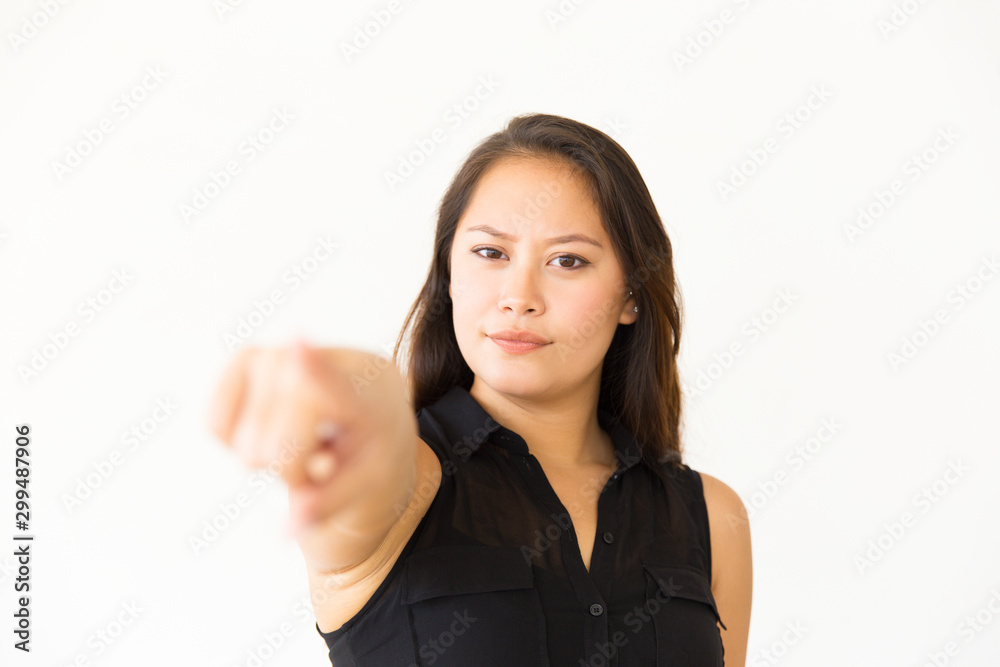 Serious woman pointing at camera. Portrait of beautiful confident young woman pointing with finger and looking at camera. Gesture concept Serious woman pointing at camera. Portrait of beautiful confident young woman pointing with finger and looking at camera. Gesture concept