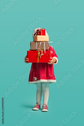 Adorable small baby girl with present box in christmas hat and red dress on the studio background