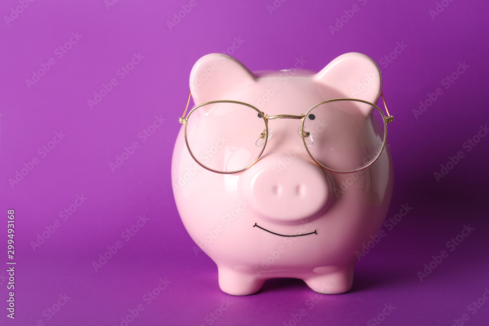 Piggy bank with eyeglasses on color background Piggy bank with eyeglasses on color background