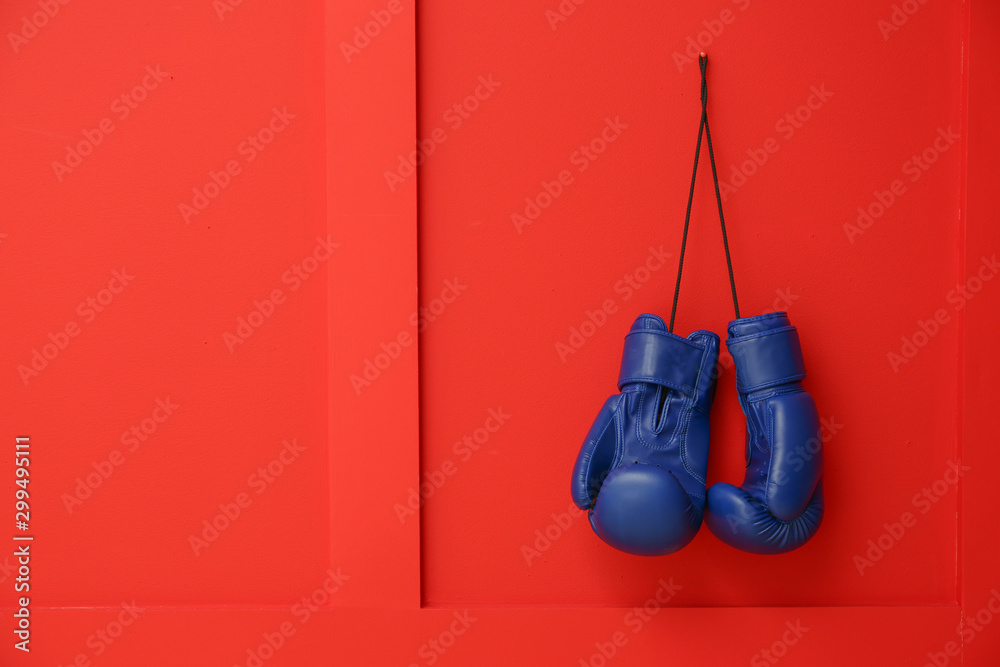 Pair of boxing gloves hanging on color wall