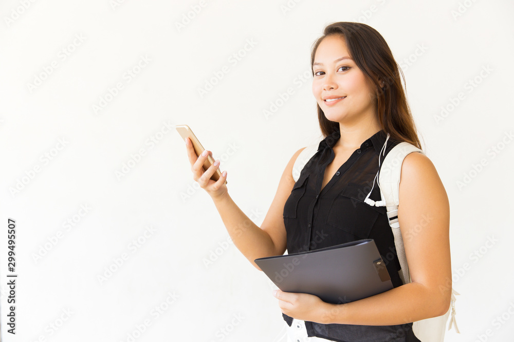 Woman with folder and smartphone smiling at camera. Portrait of beautiful young female student with backpack holding folder and using mobile phone. Technology concept Woman with folder and smartphone smiling at camera. Portrait of beautiful young female student with backpack holding folder and using mobile phone. Technology concept