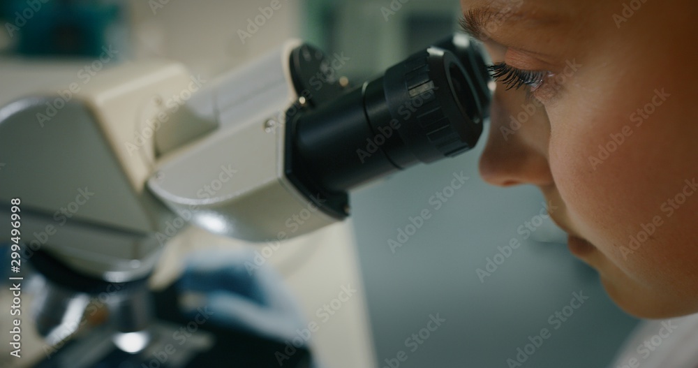 Portrait of blond female scientist is analyzing a sample to extract the DNA and molecules with microscope in laboratory.