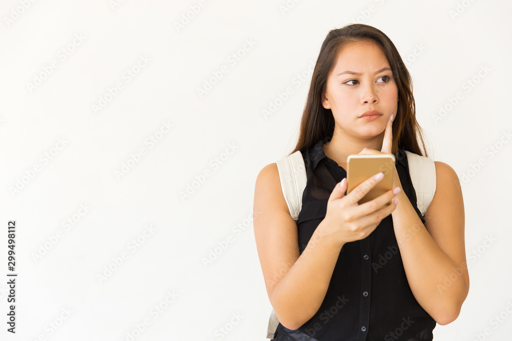 Pensive young woman using smartphone. Portrait of beautiful thoughtful young female student with backpack using mobile phone on white background. Technology concept Pensive young woman using smartphone. Portrait of beautiful thoughtful young female student with backpack using mobile phone on white background. Technology concept