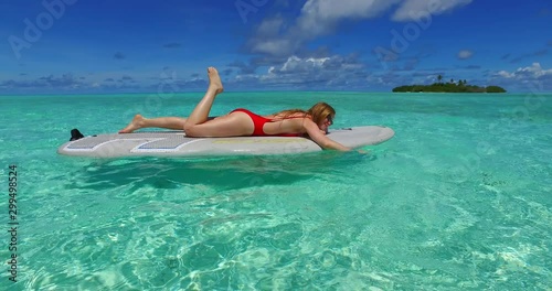 Model lying on top of a board floating in crystal clear waters in Thailand 4K photo