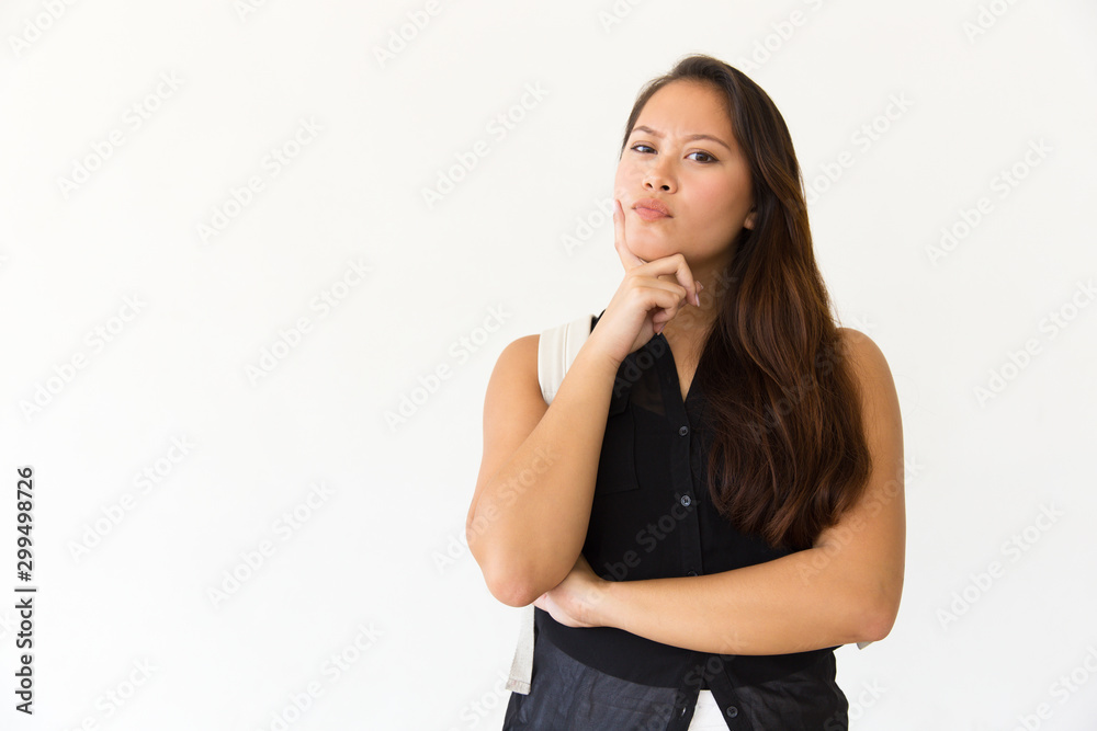 Thoughtful woman with backpack looking at camera. Portrait of beautiful pensive young woman with backpack standing with hand on chin and looking at camera on white. Facial expression concept Thoughtful woman with backpack looking at camera. Portrait of beautiful pensive young woman with backpack standing with hand on chin and looking at camera on white. Facial expression concept