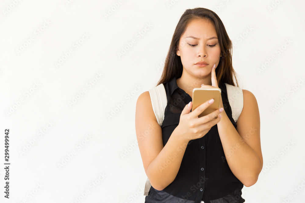 Thoughtful young woman using smartphone. Portrait of beautiful pensive young female student with backpack using mobile phone on white background. Technology concept Thoughtful young woman using smartphone. Portrait of beautiful pensive young female student with backpack using mobile phone on white background. Technology concept