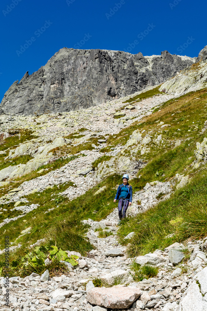 Young woman (tourist) in helmet walks down the path in the mountains. A visible peak (Baranie rohy, Baranie Rogi) in the background. High Tatras. Slovakia.