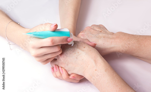 a young woman puts cream on the hands of an elderly woman from a tube