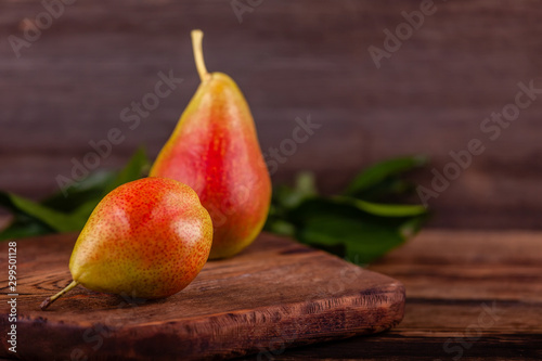 Two fresh red pears on wooden background with green leaves. Concept of healthy and vegan food. Copy space.
