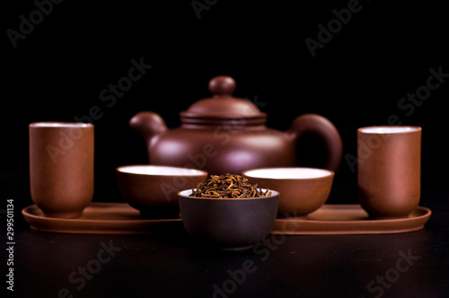 Asian tea ceremony. Clay teapot and tea cups with dry tea leaves on a black background.