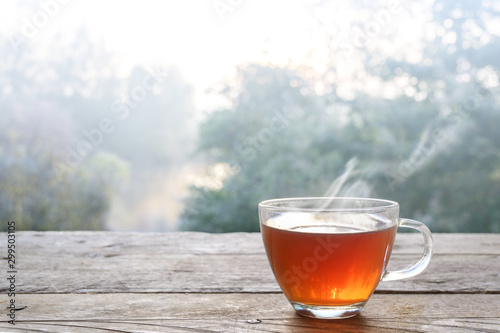 Hot steaming tea in a glass cup on a rustic wooden outdoor table on a cold foggy winter day, copy space, selected focus, narrow depth of field