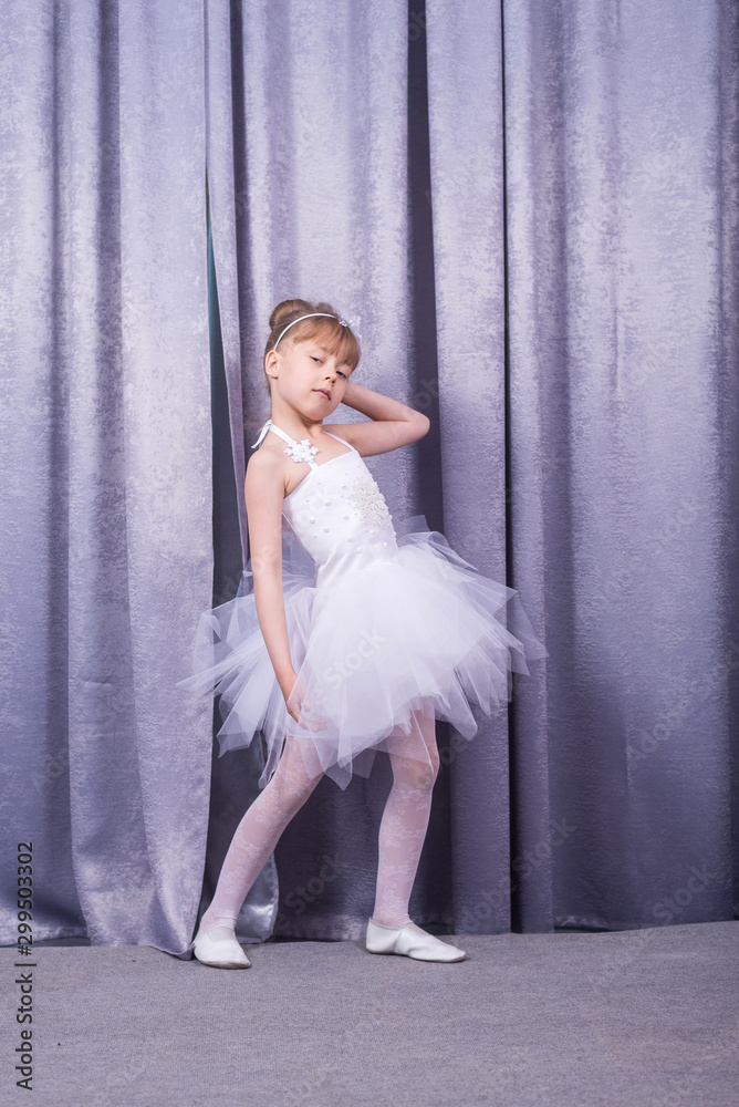 Little cute girl in a white dress on the background of theatrical curtains.