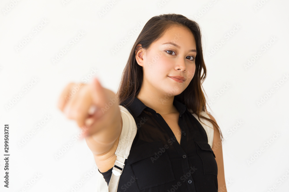 Pensive smiling teenage girl pointing finger at camera. Young Latin woman standing isolated over white background. Choosing you concept Pensive smiling teenage girl pointing finger at camera. Young Latin woman standing isolated over white background. Choosing you concept