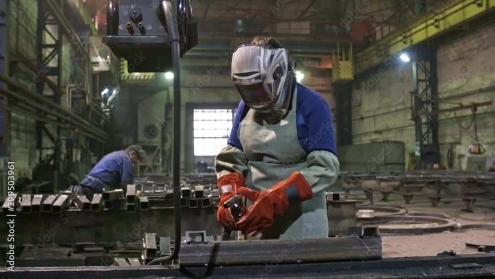 Tracking shot shot of female worker in gloves putting on safety helmet and welding steel part at metal fabrication facility Tracking shot shot of female worker in gloves putting on safety helmet and welding steel part at metal fabrication facility