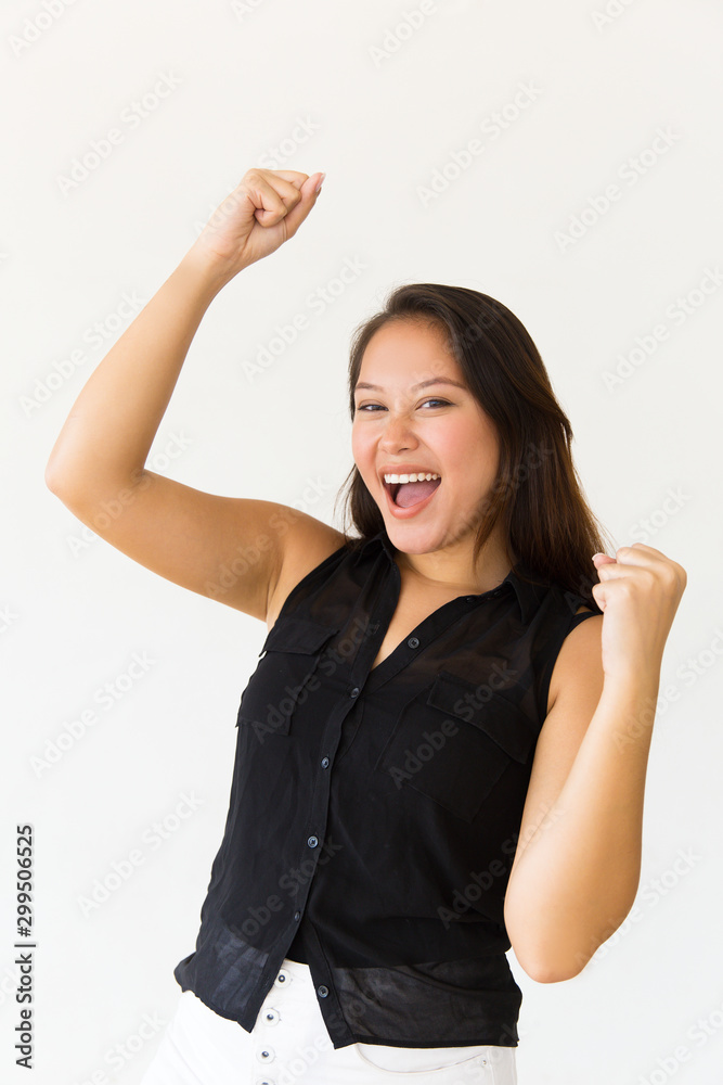 Excited young woman raising fists. Portrait of beautiful cheerful young woman celebrating and smiling at camera. Winner concept Excited young woman raising fists. Portrait of beautiful cheerful young woman celebrating and smiling at camera. Winner concept