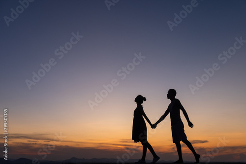 Silhouettes of happy young couple against the sunset sky,walking