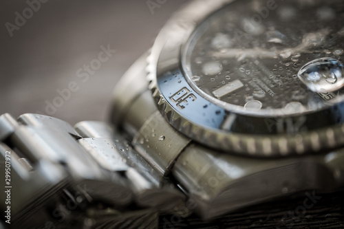 Close-up, shallow focus of a luxury, Swiss manufactured men's mechanical diving watch showing droplets of water on the face and strap.