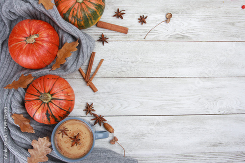 Grey mug of coffee, wrapped in wool plaid or scarf, spices, dry oak leaves, acorns, orange pumpkins on white wooden table. Autumn drink concept. Fall, spicy latte, thanksgiving, top, copy space
