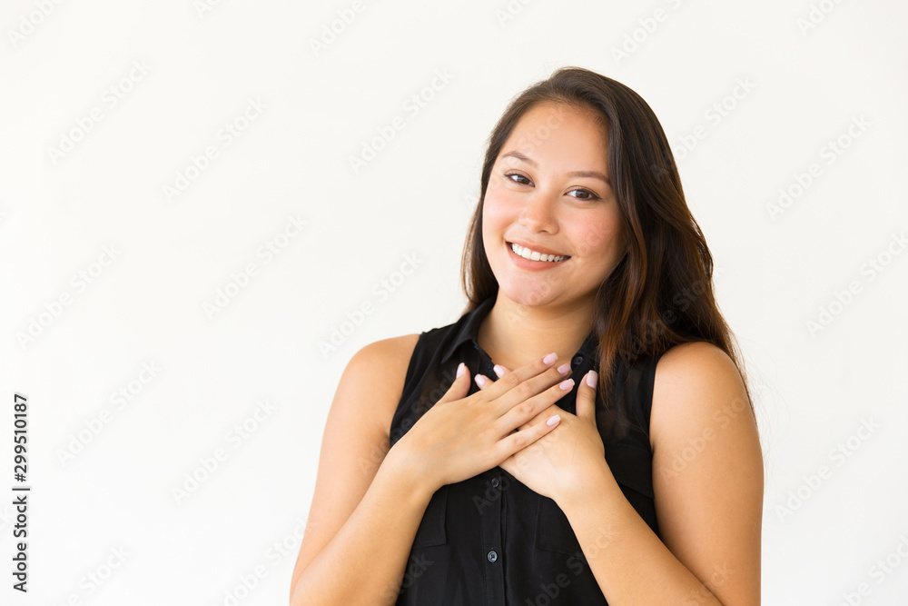 Content woman with hands on chest. Beautiful happy young woman holding hands near heart and smiling at camera. Gesture concept Content woman with hands on chest. Beautiful happy young woman holding hands near heart and smiling at camera. Gesture concept