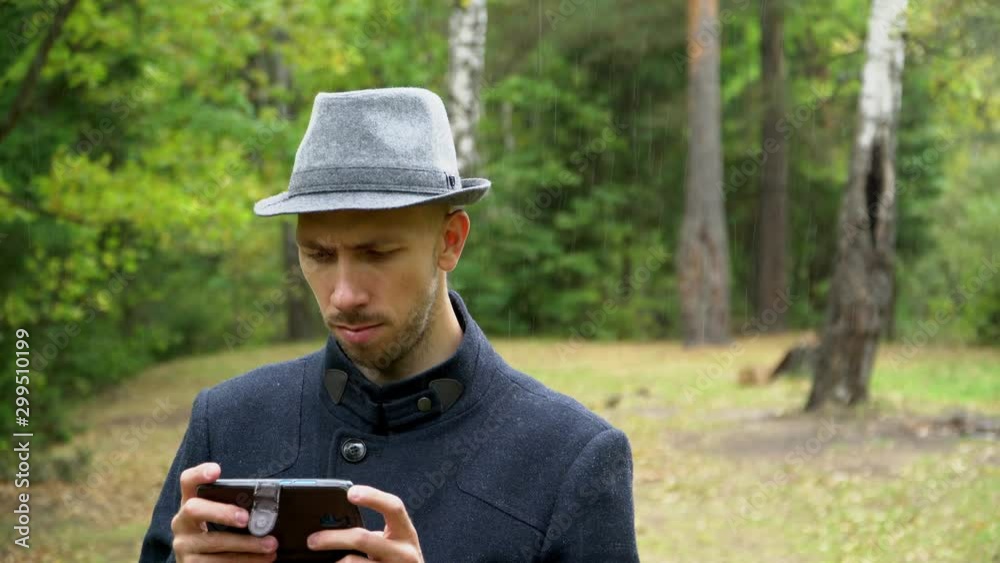 A man in a hat and coat in the rain looking at something in the phone A man in a hat and coat in the rain looking at something in the phone
