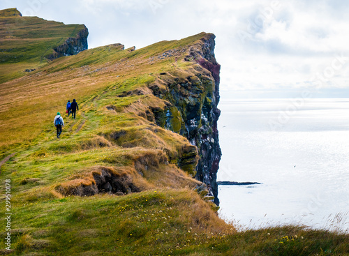 sharp cliff with people, clouds and ocean in iceland