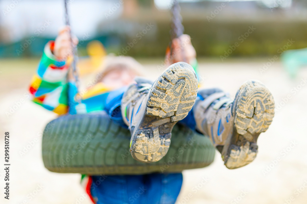 Funny kid boy having fun with chain swing on outdoor playground. child  swinging on warm sunny spring or autumn day. Active leisure with kids.  Selective focus, no face of kid. Stock Photo