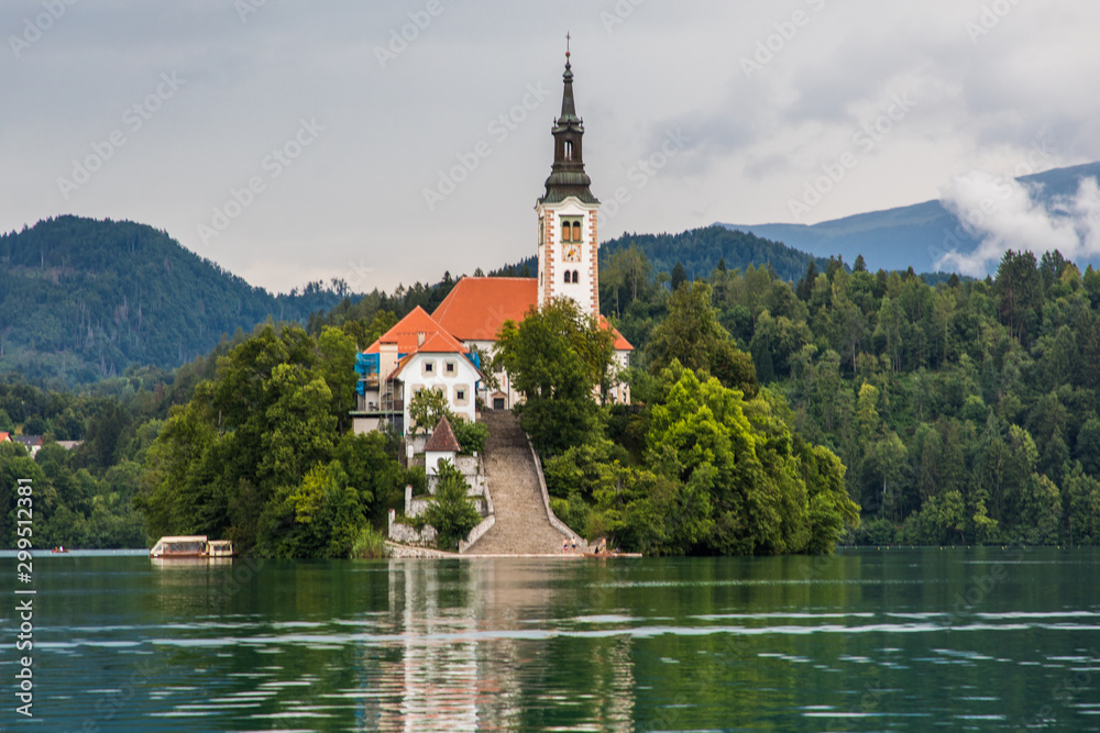 Bled, Slovenia - July, 2019: Lake Bled with St. Marys Church of Assumption on small island. Mountains and valley on background. Space for your text. Bled, Slovenia - July, 2019: Lake Bled with St. Marys Church of Assumption on small island. Mountains and valley on background. Space for your text.