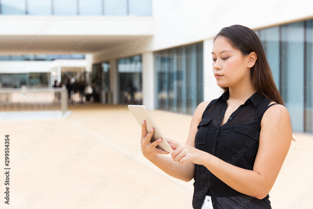 Focused student girl reading on tablet screen. Young Latin woman standing outside, using digital device. Wireless internet connection concept Focused student girl reading on tablet screen. Young Latin woman standing outside, using digital device. Wireless internet connection concept