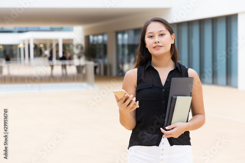 Fotografía Pensive female student holding notebooks and papers, texting message