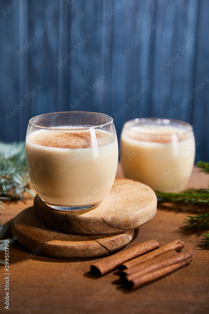 delicious eggnog cocktail on round wooden boards near spruce branches and cinnamon sticks on blue textured background delicious eggnog cocktail on round wooden boards near spruce branches and cinnamon sticks on blue textured background