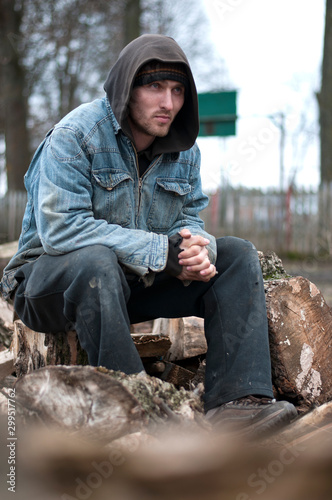 Homeless, sad man in a beanie sitting outside and feeling cold, trying to warm up his hands