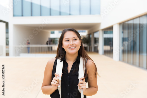 Free Download Happy excited female tourist walking outside. Young mix raced woman in casual standing near city building, holding backpack straps, looking away, smiling. Tourist in city concept - GFXLoad