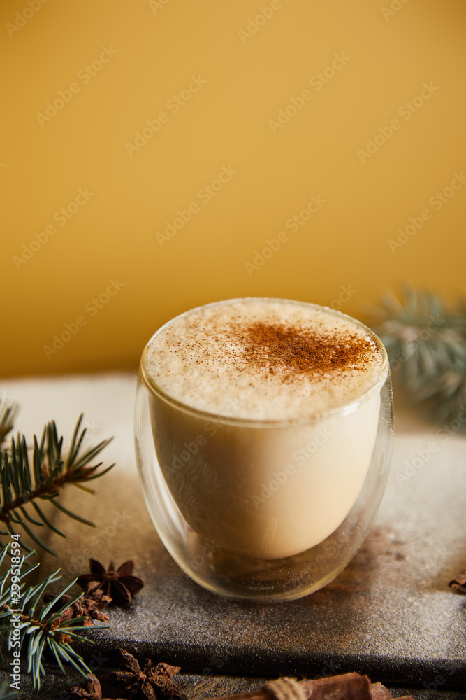 traditional eggnog cocktail with cinnamon near spruce branches and scattered sugar powder on orange background - obrazy, fototapety, plakaty 