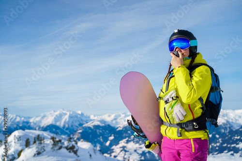Photo of woman in helmet and with snowboard talking on walkie-talkie standing at ski resort
