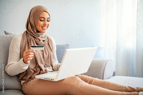 Gorgeous young woman using laptop at home shopping online. Muslim woman wearing hijab using laptop and holding credit card. Internet banking concept. Muslim woman online shopping