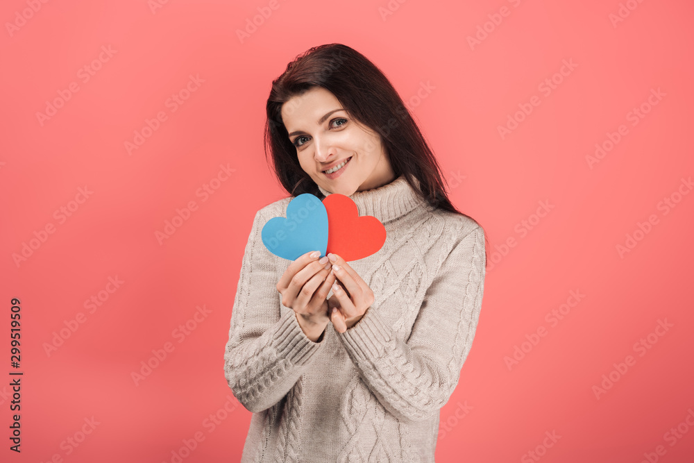happy woman in sweater holding blue and red heart-shaped paper artwork on pink happy woman in sweater holding blue and red heart-shaped paper artwork on pink