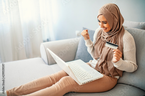 Gorgeous young woman using laptop at home shopping online. Muslim woman wearing hijab using laptop and holding credit card. Internet banking concept. Muslim woman online shopping