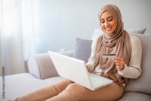 Content Arab Woman Shopping Online Being At Home. Online shopping. Beautiful young muslim woman showing a credit card with laptop. Smiling young muslim girl online shopping at home