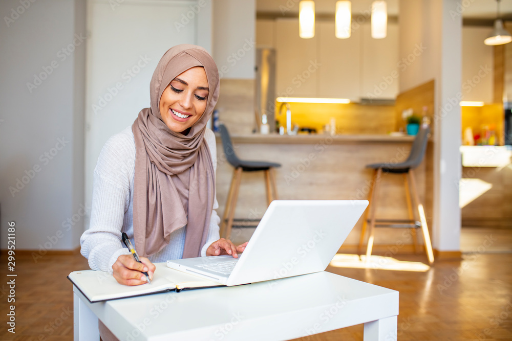 Pretty woman wearing hijab in front of laptop search and doing office work with different face expression isolated in home background - office, business, finance and work station concept