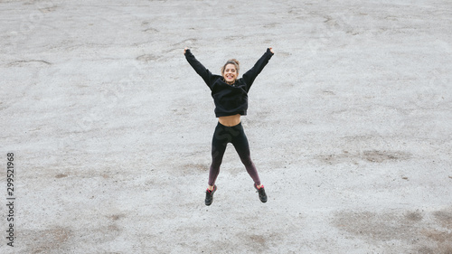 Fitness lifestyle and workout success concept. Happy woman jumping and raising arms on a road. Runner celebrating training goals.